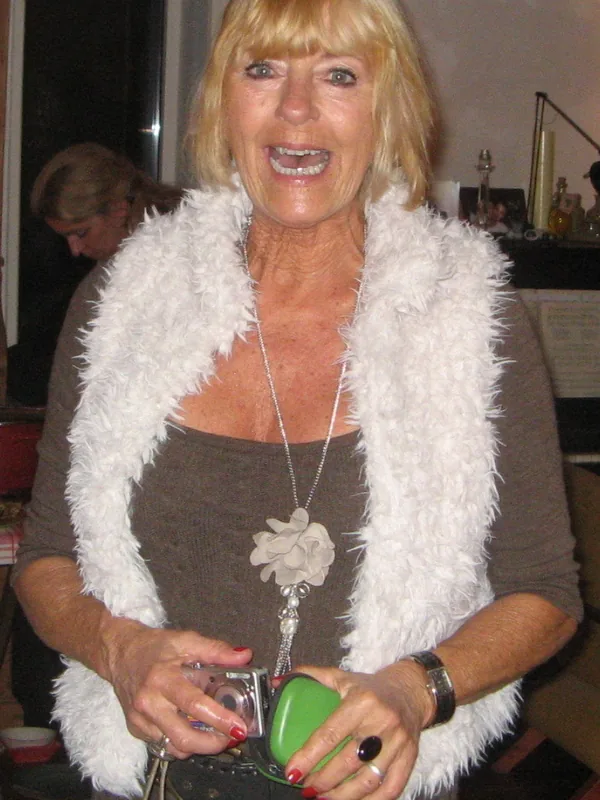 Portrait d'une femme blonde souriante portant une écharpe blanche et tenant un appareil photo et un objet vert.