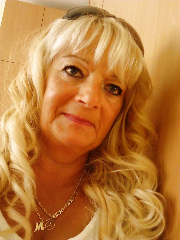 Portrait d'une femme aux cheveux blonds bouclés, regardant l'objectif, avec des lunettes de soleil sur la tête et un collier orné.