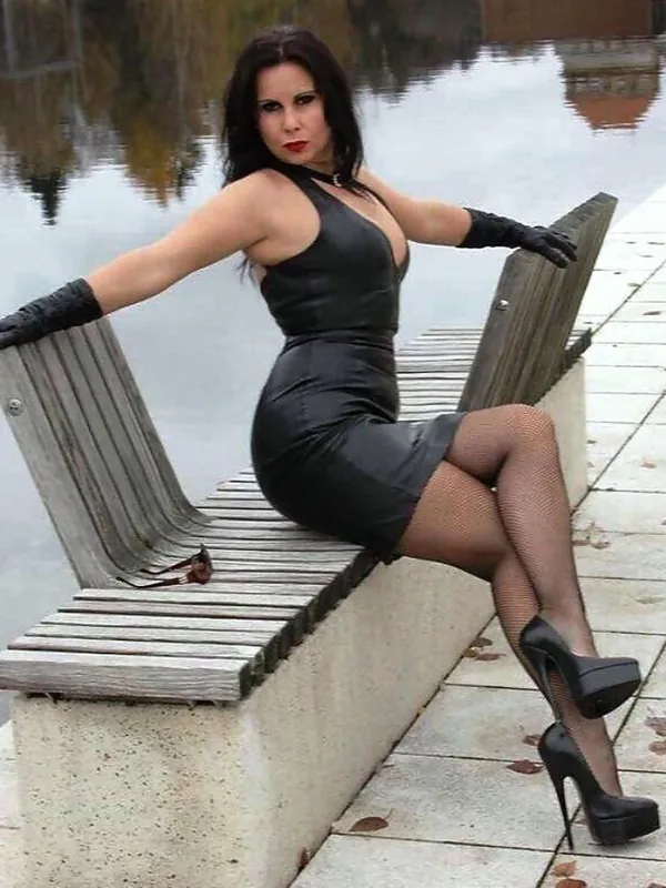 Femme en robe noire et collants à mailles assise sur un banc en bois près d'un lac, regardant l'objectif.